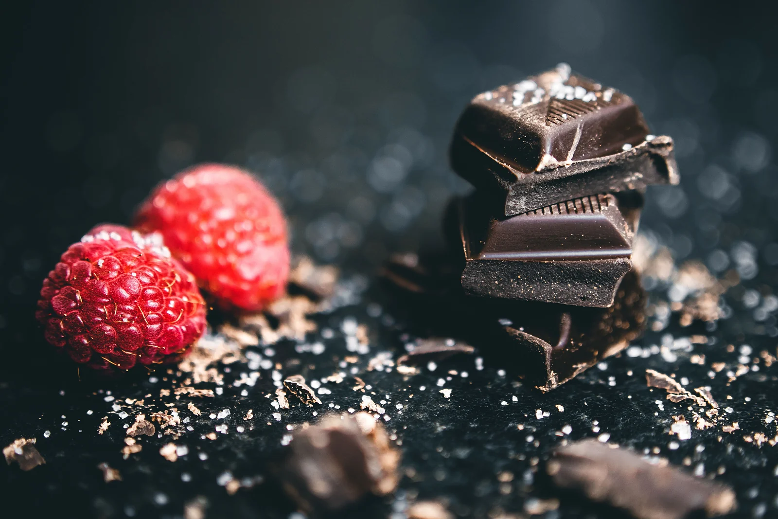 Шматочки темного шоколаду й свіжа малина на темному тлі з какао-крихтою